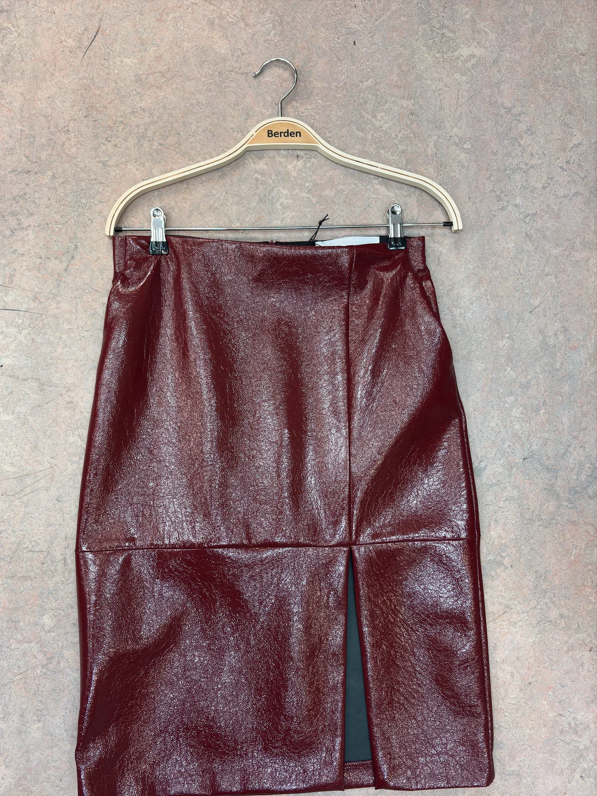 Burgundy patent leather skirt on a hanger, photographed on a concrete floor