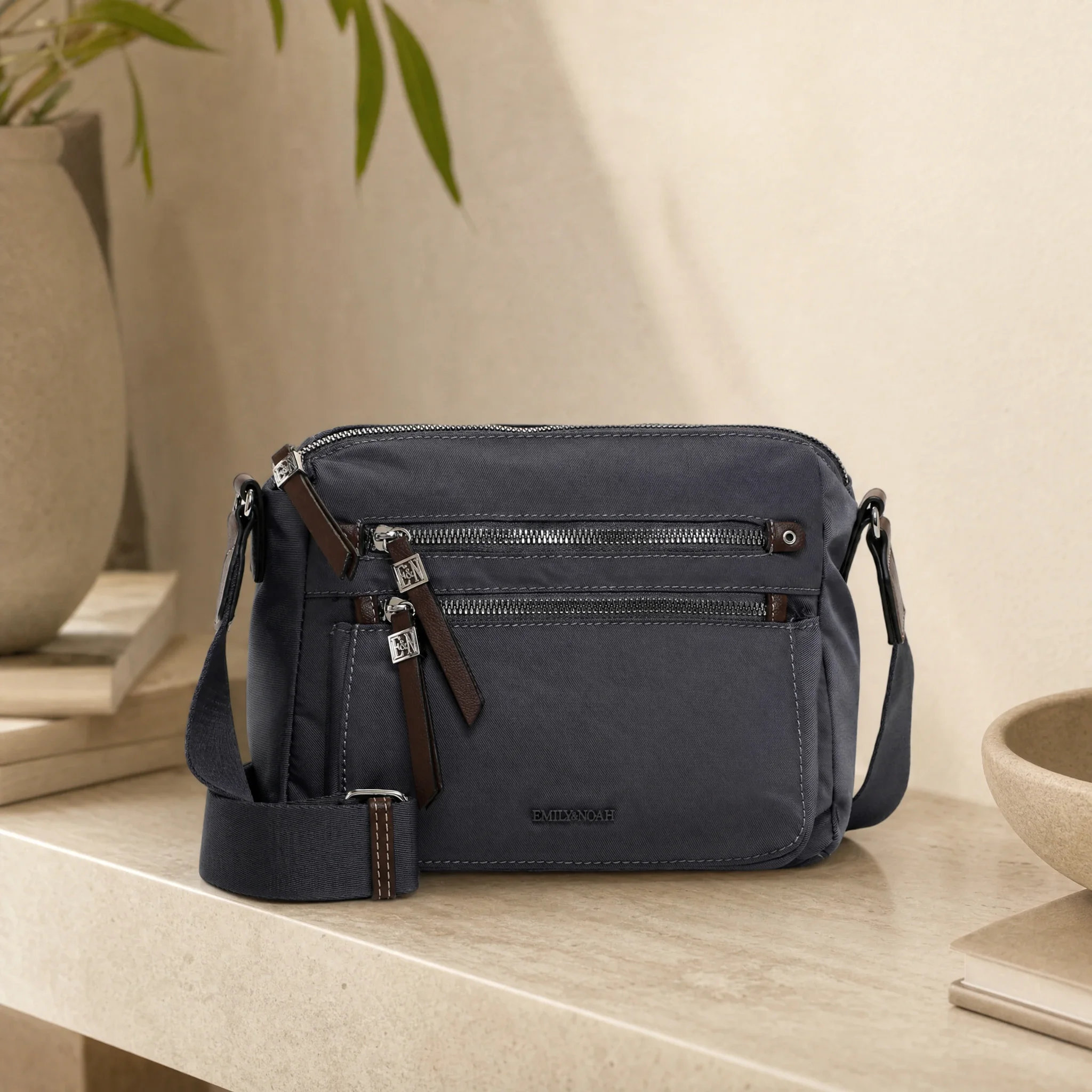Lifestyle image: gray crossbody bag with zip pockets on a light stone table