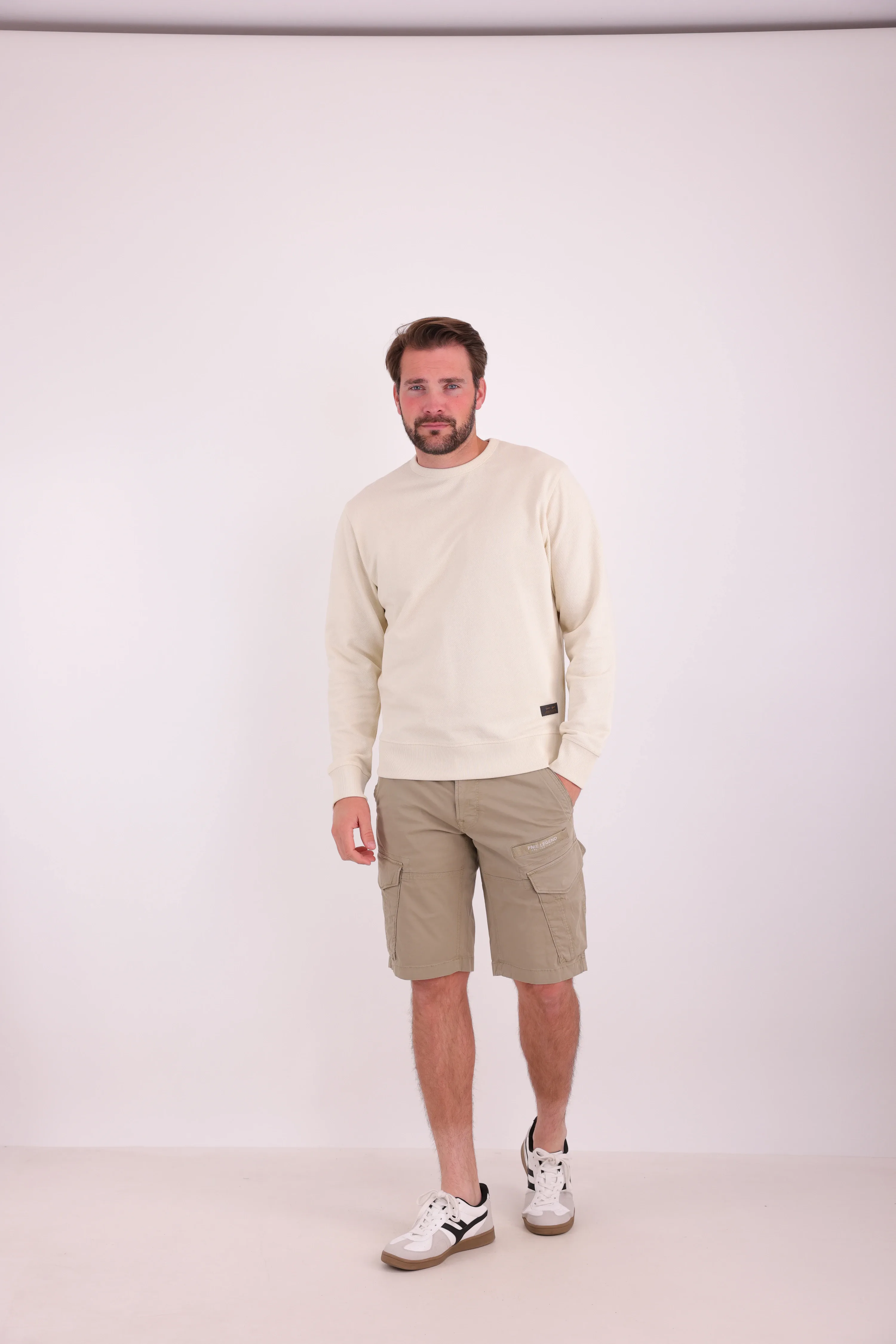 Studio photo of a model in a cream-colored sweater and beige cargo shorts